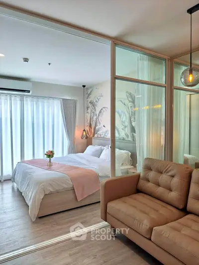 Modern bedroom with glass partition and cozy seating area, featuring elegant decor and natural light.