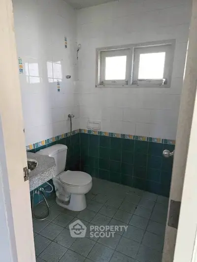 Spacious bathroom with tiled walls and floor, featuring a modern toilet and natural light from windows.