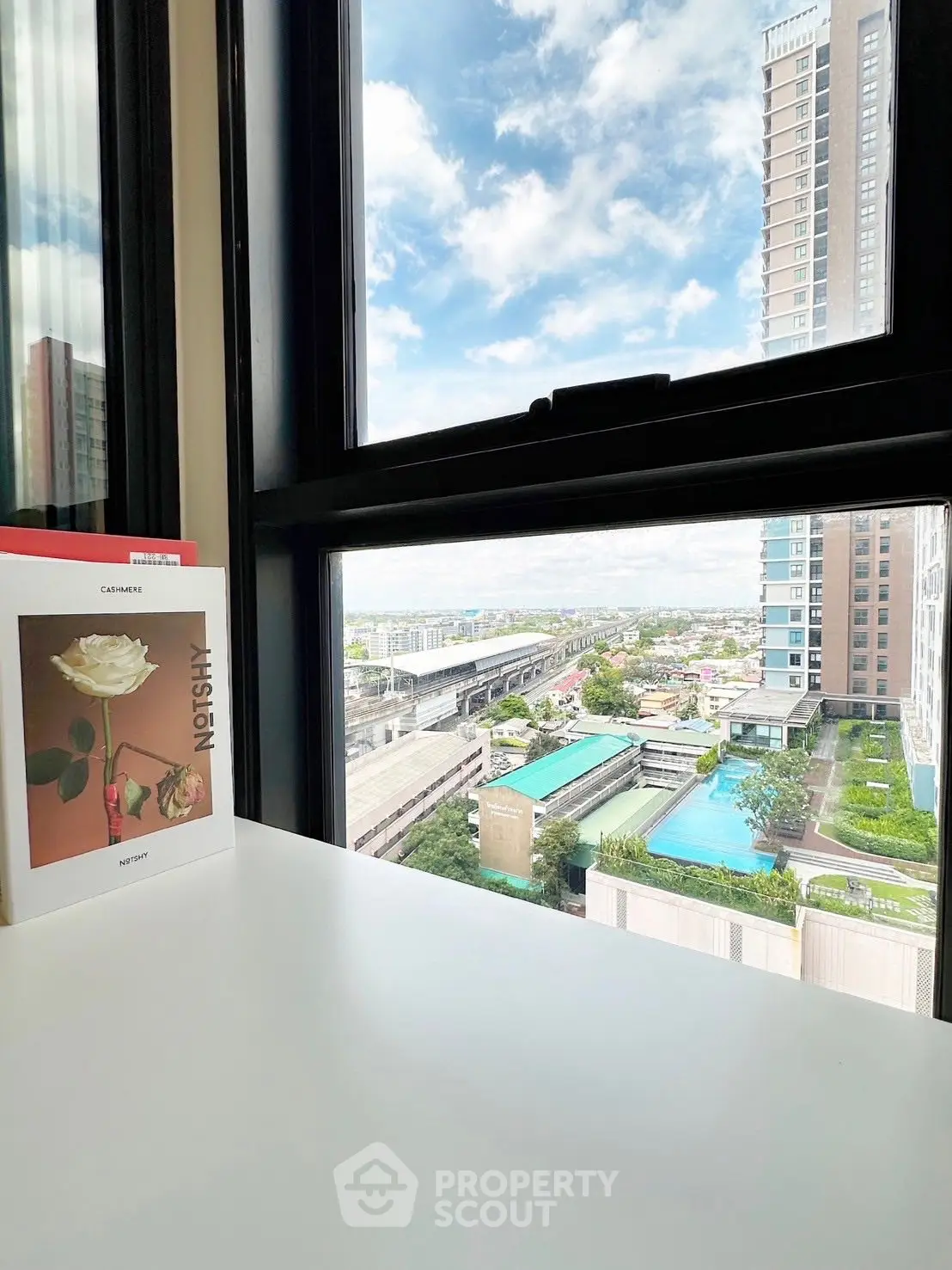 Stunning urban view from a modern high-rise window overlooking a pool and cityscape.