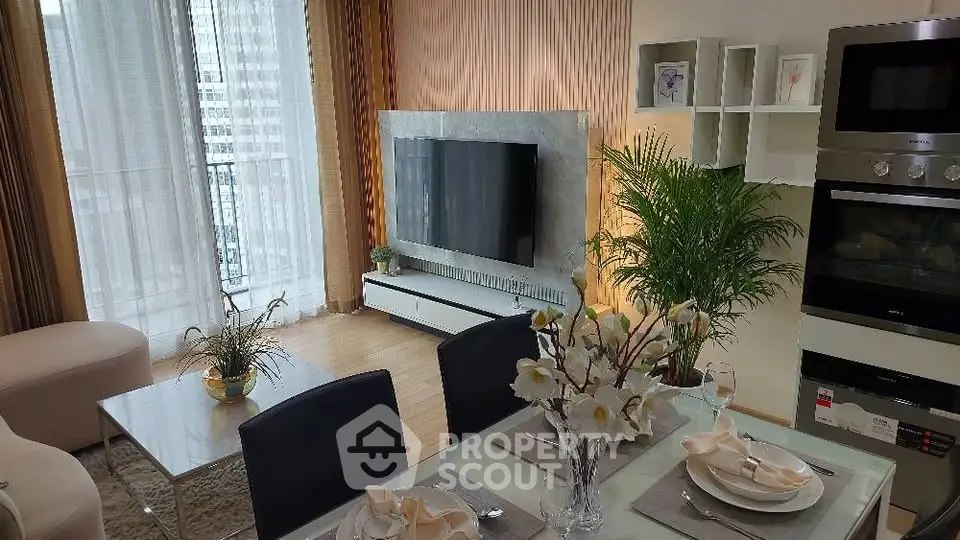 Modern living room with elegant dining area and large TV, featuring stylish decor and natural light.