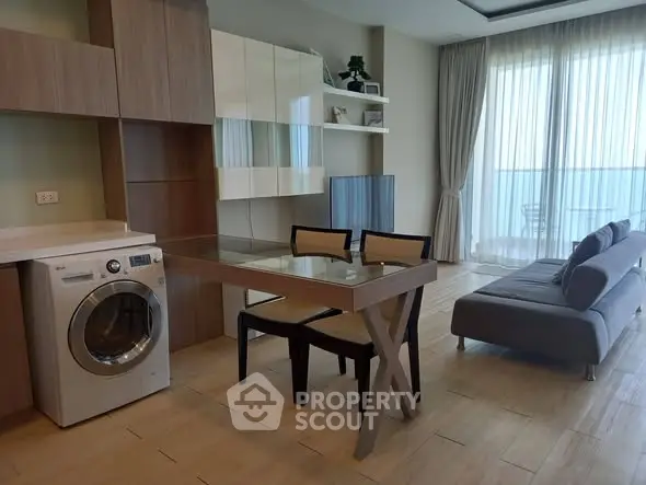 Modern living room with washing machine, glass dining table, and balcony view.