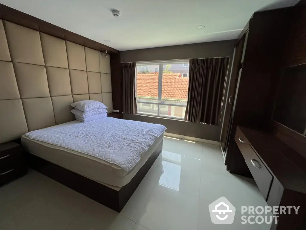 Spacious bedroom with large windows offering ample natural light, featuring a comfortable bed, sleek flooring, and elegant dark wood furniture.