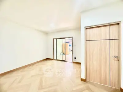 Spacious empty room with wooden flooring and sliding glass doors leading to a balcony.