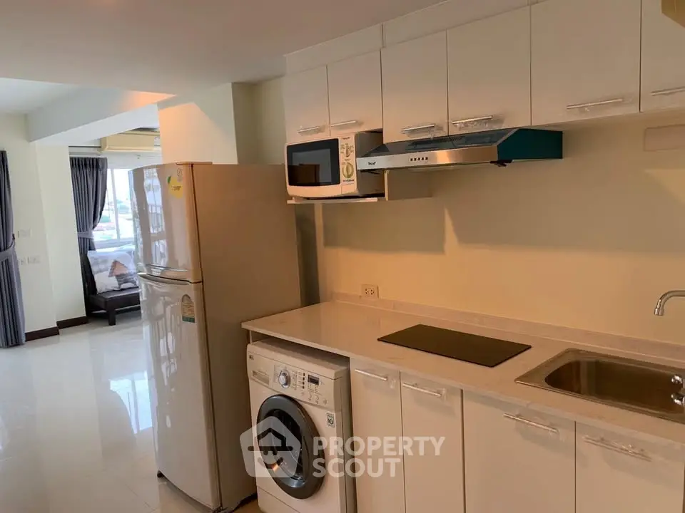 Modern kitchen with appliances including washing machine and microwave in a bright apartment.