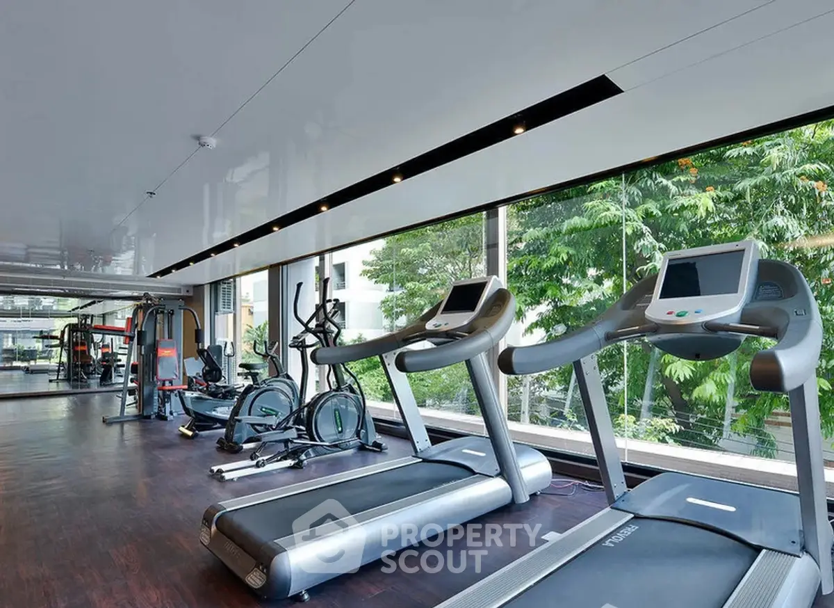 Modern gym with treadmills and exercise equipment in a bright, spacious room with large windows.