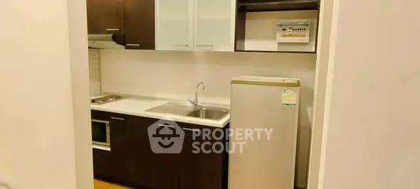 Modern kitchen with dark wood cabinets and stainless steel appliances in cozy apartment.