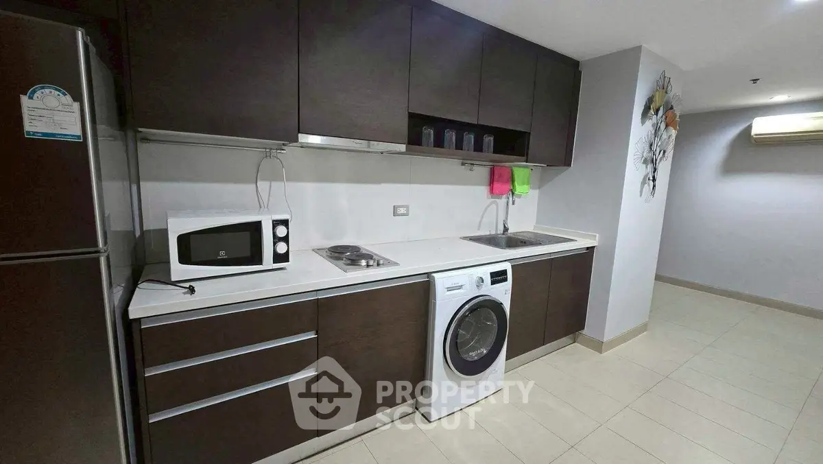 Modern kitchen with dark cabinets, washing machine, and microwave in sleek apartment.