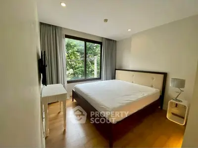 Spacious bedroom with large window and modern furnishings in a serene setting.