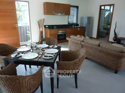 Modern open-plan living room with stylish dining area and kitchen, featuring wicker chairs and sleek appliances.