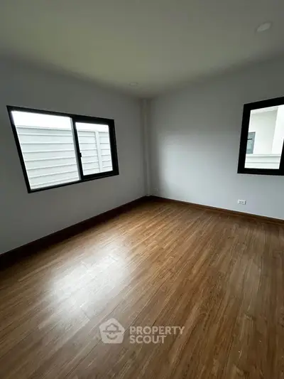 Spacious empty room with wooden flooring and large windows, perfect for customization.