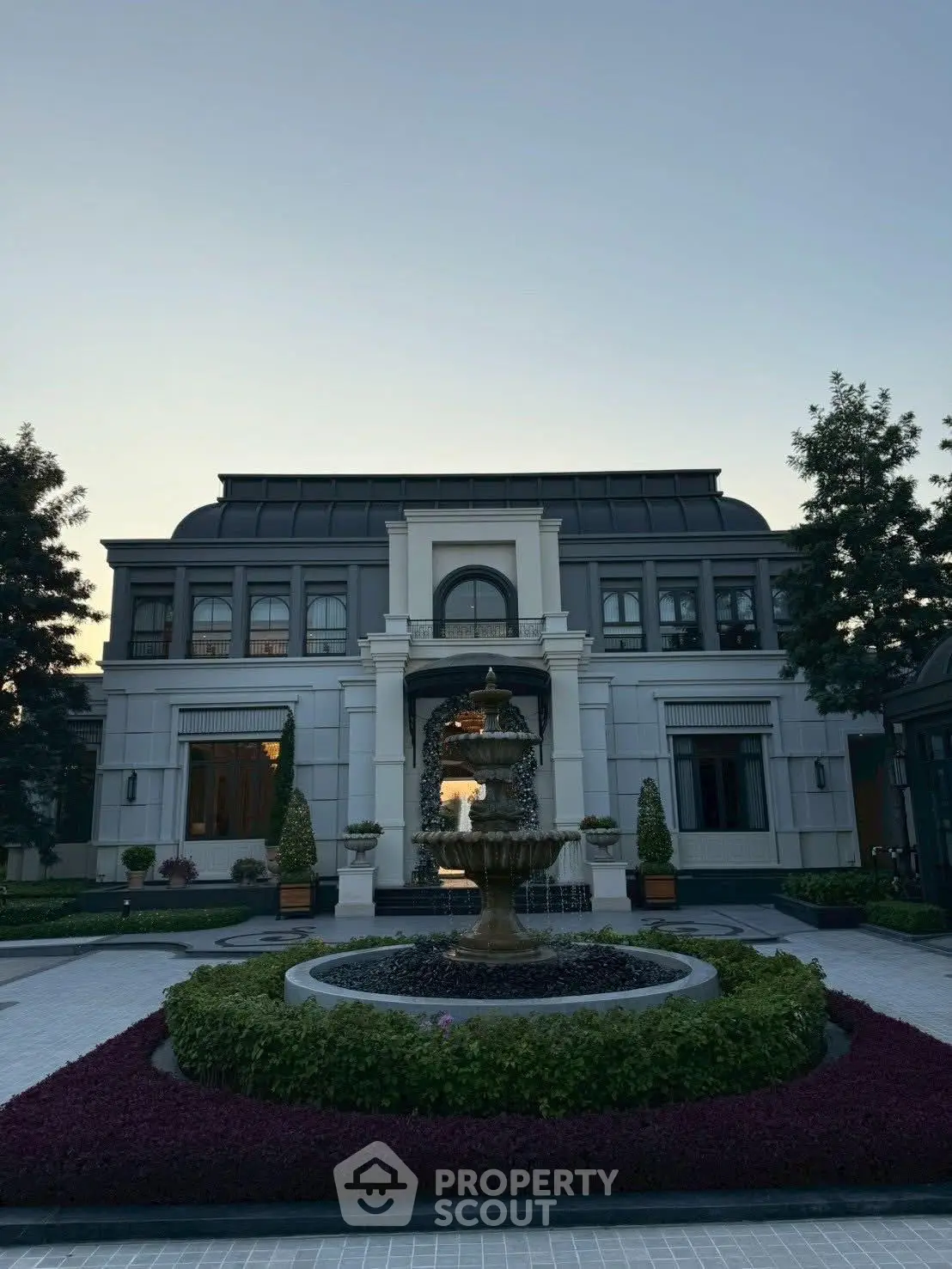 Luxurious mansion exterior with elegant fountain and manicured garden at sunset.