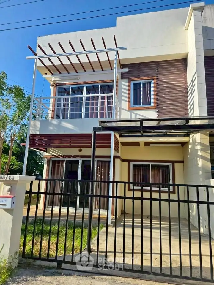 Modern two-story house with balcony and gated driveway in a sunny neighborhood.
