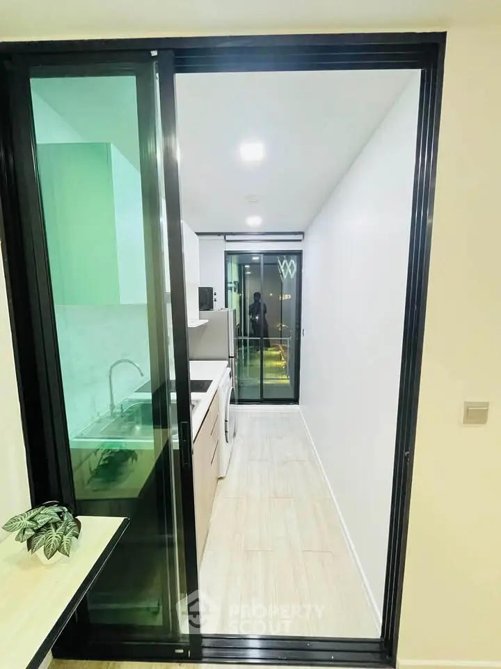 Modern kitchen with sleek design and sliding glass doors leading to a balcony, featuring a washing machine and compact layout.