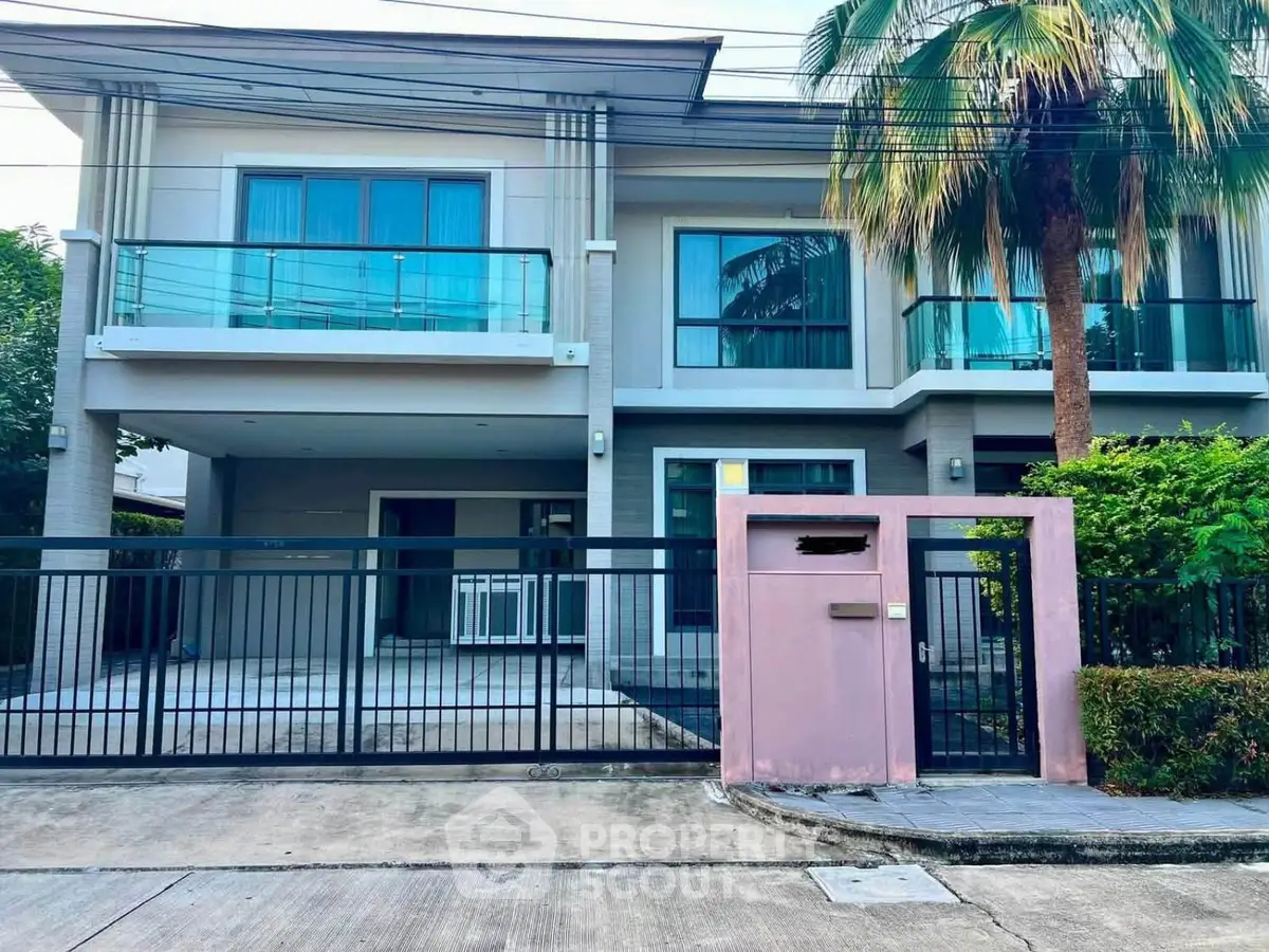 Modern two-story house with spacious balcony and gated entrance in a serene neighborhood.