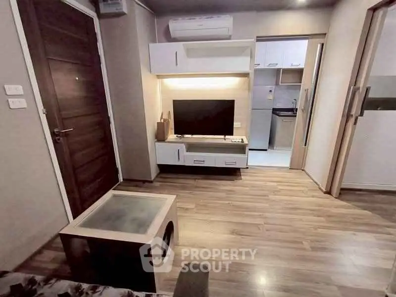 Modern living room with wooden flooring and sleek furniture adjacent to a compact kitchen.