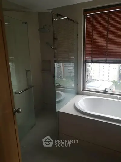 Modern bathroom with glass shower and bathtub, featuring city view through window.