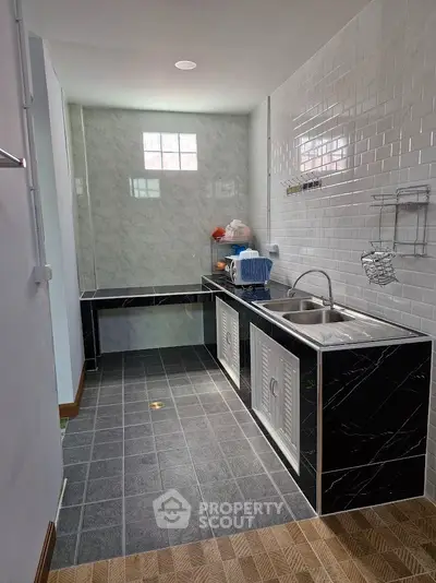 Modern kitchen with sleek black countertops and white tiled walls, featuring a double sink and ample storage space.