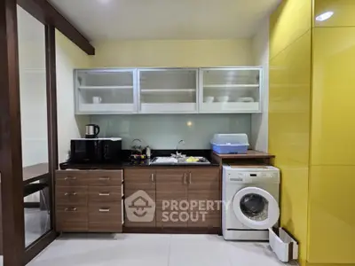 Modern kitchen with sleek cabinets, washing machine, and microwave in a compact layout.