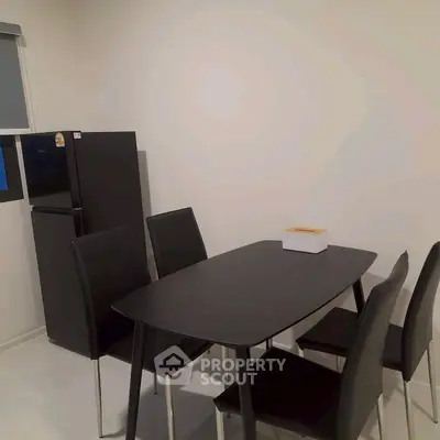 Modern dining area with sleek black table and chairs, adjacent to a compact refrigerator.