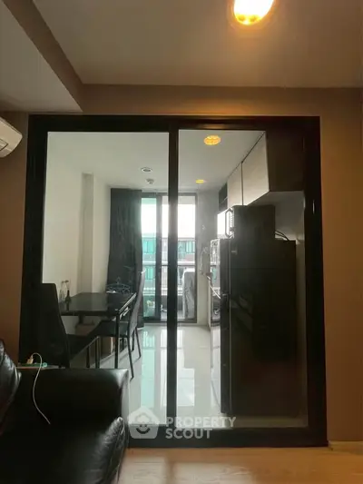 Modern apartment with glass partition separating living room and kitchen area, featuring sleek furniture.