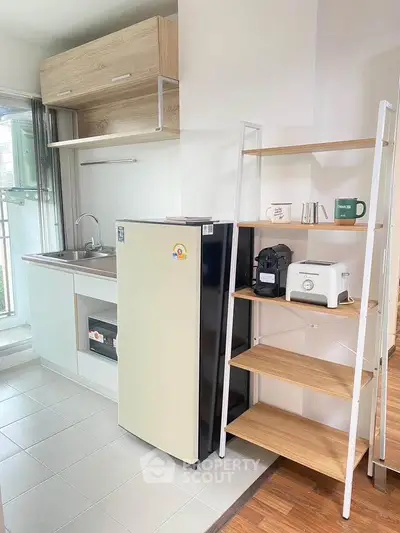 Modern compact kitchen with fridge, sink, and open shelving in a bright apartment.