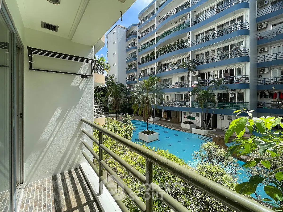 Charming balcony view overlooking a modern apartment complex with a sparkling pool and lush greenery.