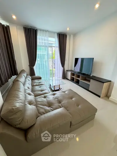 Modern living room with large sofa and flat-screen TV, featuring floor-to-ceiling windows and elegant curtains.
