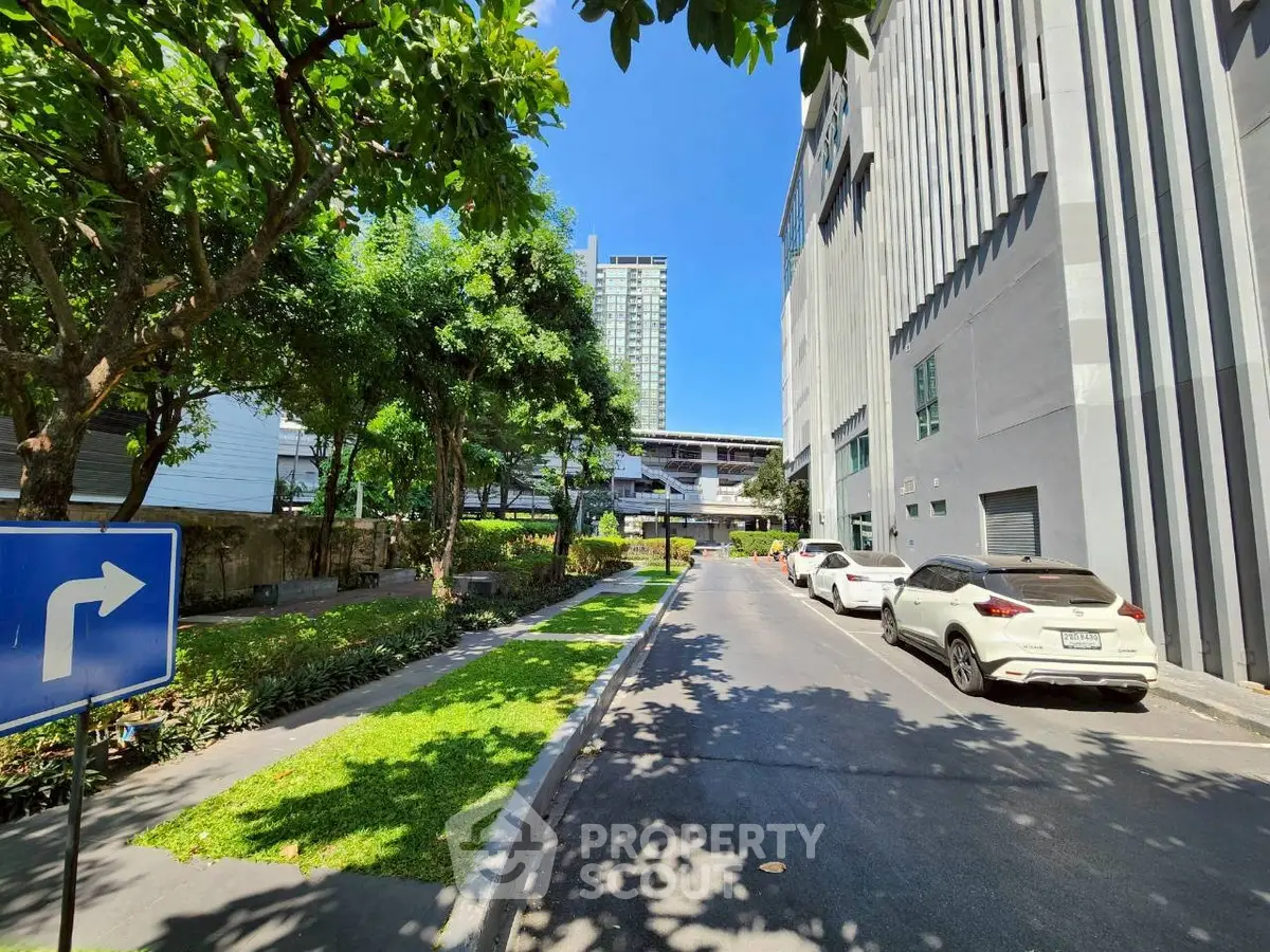 Modern urban building exterior with lush greenery and parked cars on a sunny day.
