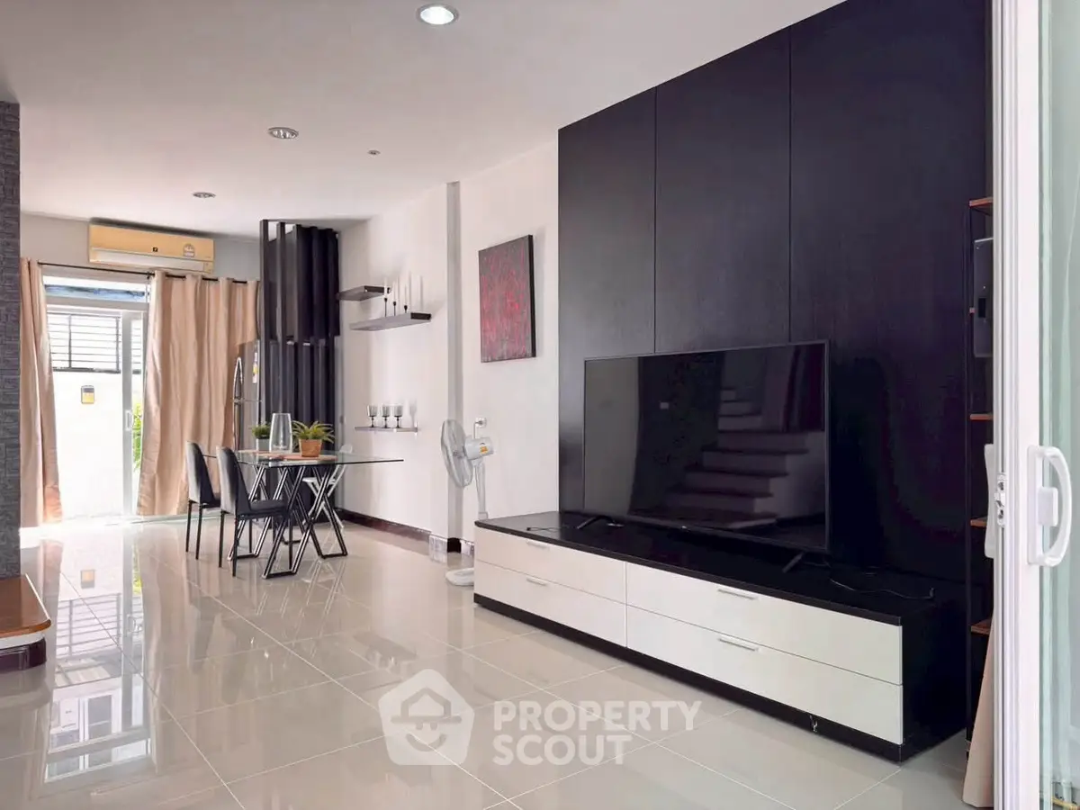 Modern living room with sleek TV unit and dining area, featuring elegant decor and ample natural light.