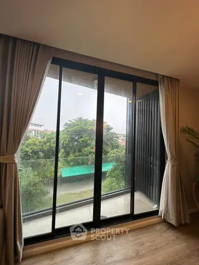 Spacious balcony with large glass doors offering a serene view of lush greenery and a river.