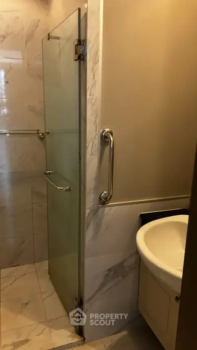 Compact bathroom with glass shower door and modern sink in elegant marble setting.