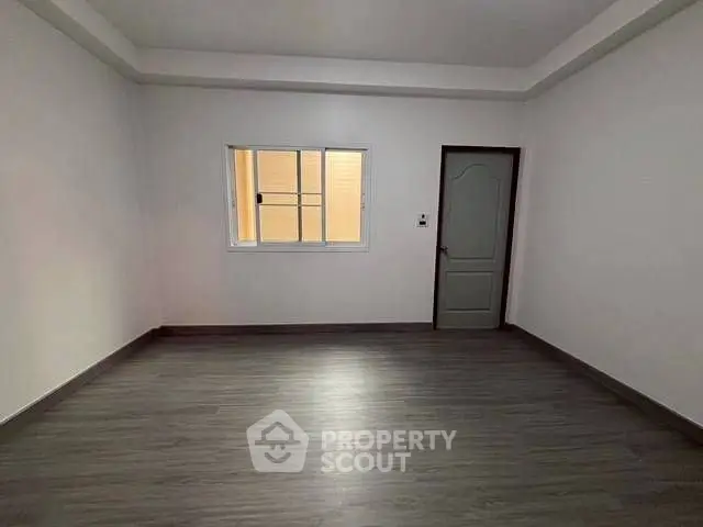 Spacious empty room with modern flooring and window, ideal for customization.