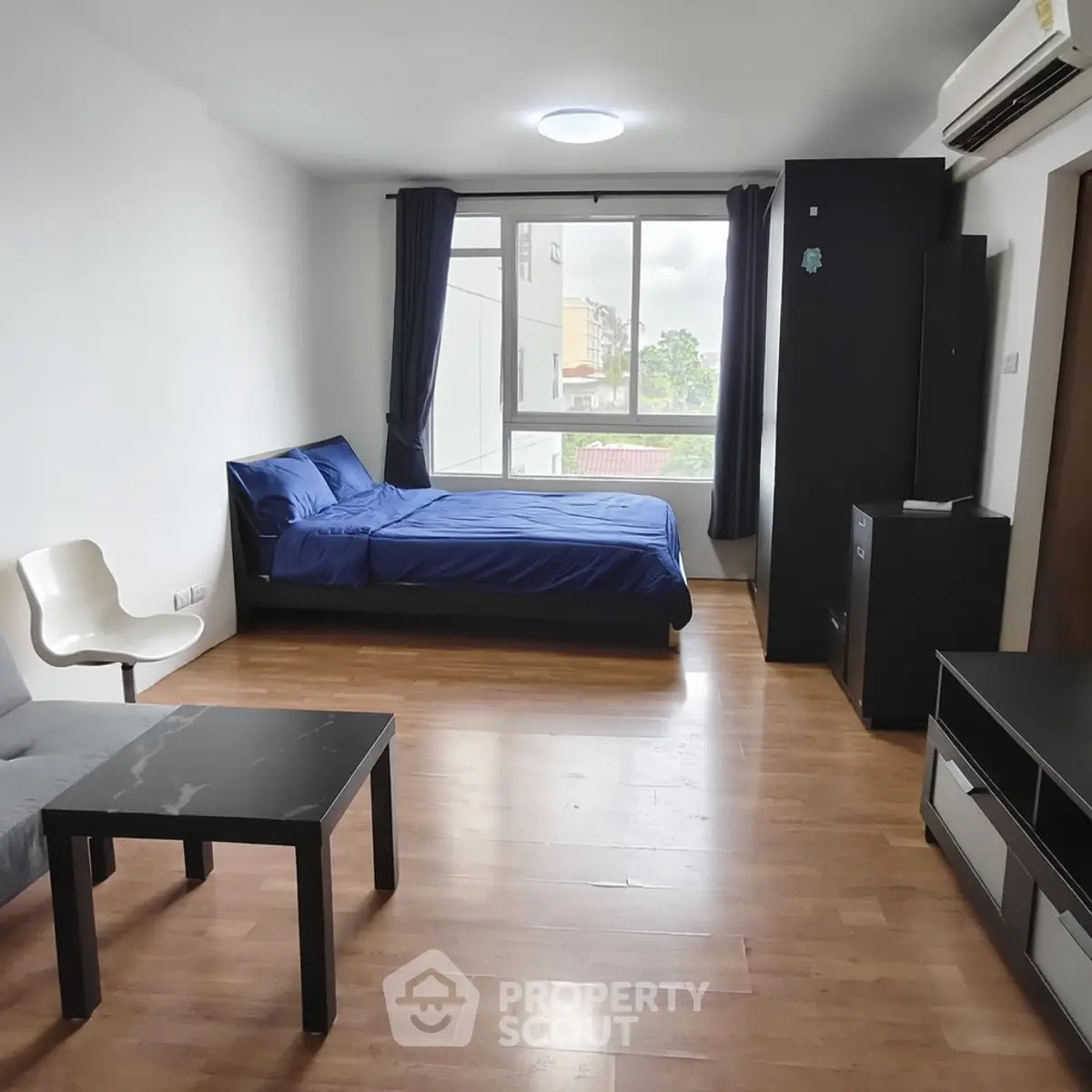 Spacious modern bedroom with wooden flooring and large window view.
