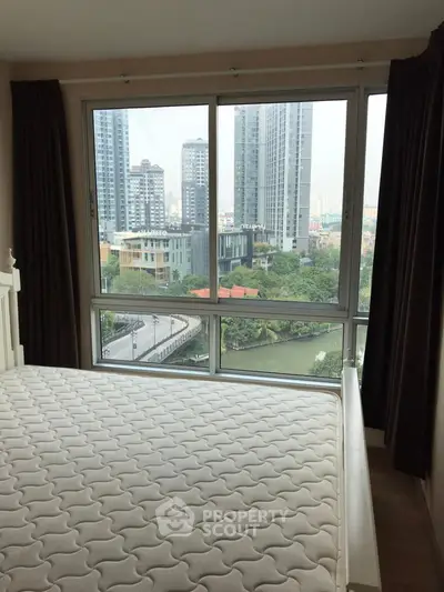 Spacious bedroom with large window offering stunning cityscape view.