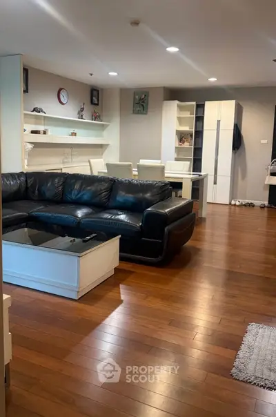 Spacious living room with modern black leather sofa and elegant wooden flooring.
