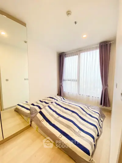 Cozy bedroom with large window and mirrored wardrobe, featuring elegant curtains and wooden flooring.