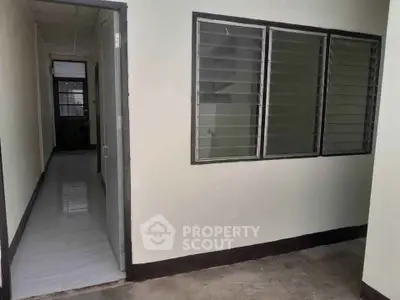 Simple interior hallway with open door and louvered windows, showcasing minimalist design.