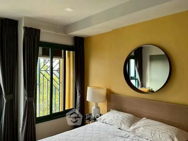 Cozy bedroom with yellow accent wall and round mirror, featuring large windows and elegant curtains.