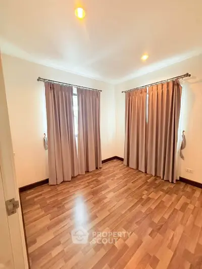 Spacious empty bedroom with wooden flooring and large windows, perfect for customization.