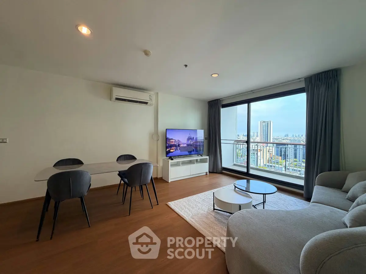 Spacious living room with city view, modern furniture, and large windows in a high-rise apartment.