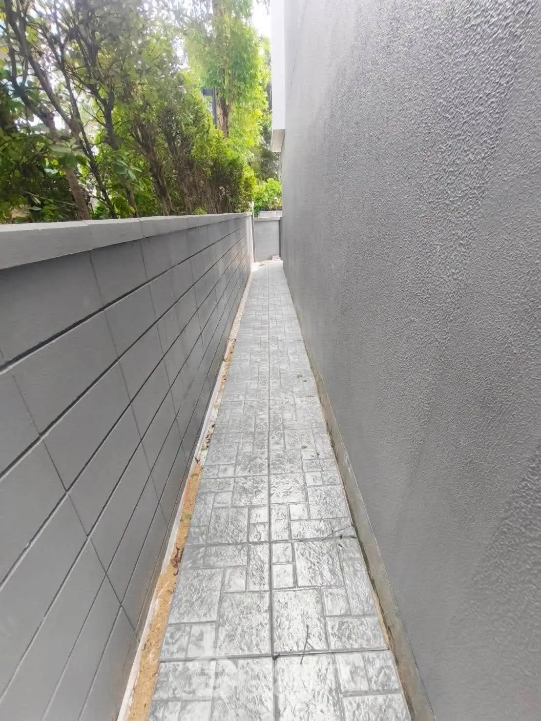 Narrow outdoor pathway with modern gray walls and textured paving stones.