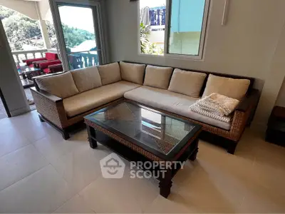Spacious living room with elegant wicker sofa and glass coffee table, opening to a scenic balcony view.