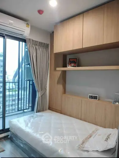 Modern bedroom with balcony view, featuring built-in wooden shelves and air conditioning.