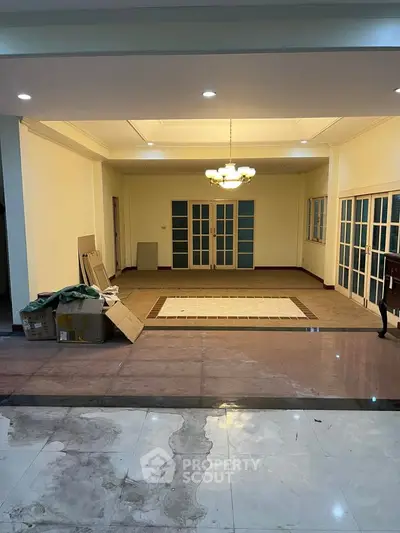 Spacious living room with elegant chandelier and large windows, perfect for family gatherings.