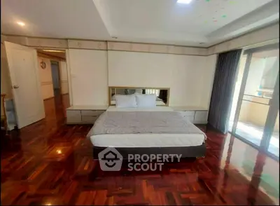 Spacious bedroom with hardwood floors and balcony access in a modern apartment.