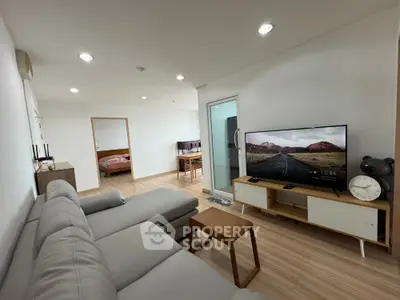 Modern living room with sleek furniture and large TV, open layout leading to bedroom