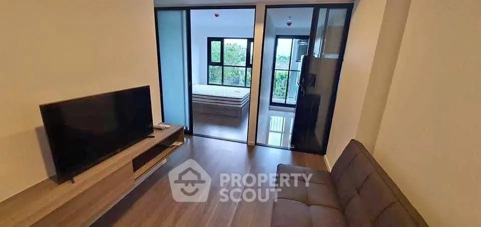 Modern apartment living room with TV and view into bedroom, featuring sleek wooden flooring.