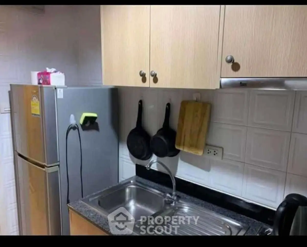 Modern kitchen with stainless steel sink and fridge, wooden cabinets, and hanging pans.