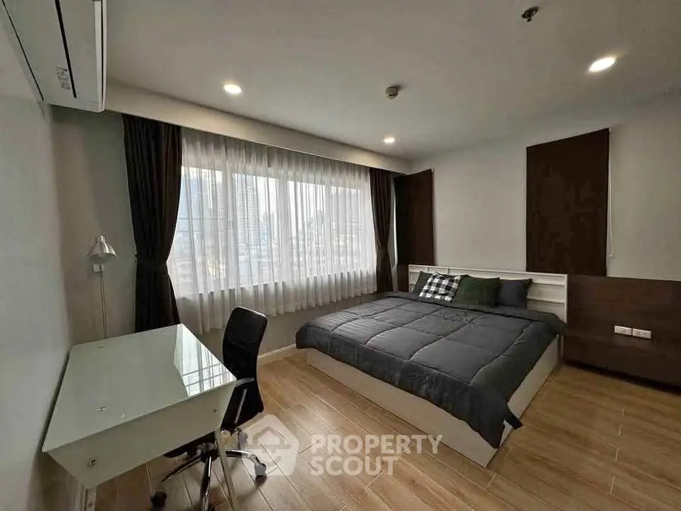 Modern bedroom with city view, featuring a sleek desk and comfortable bed, ideal for urban living.