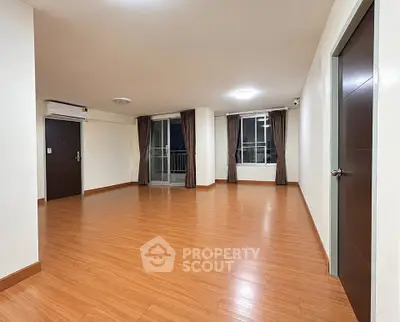 Spacious empty living room with wooden flooring and large windows in modern apartment.